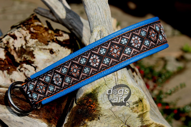 May include: A blue leather dog collar with a black and brown patterned fabric insert. The collar has a silver D-ring.