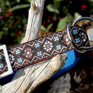 May include: A black and orange dog collar with a silver buckle and a silver D-ring. The collar features a geometric pattern with brown, white and blue accents.