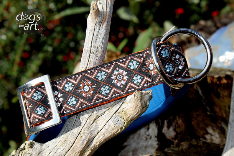 May include: A black and orange dog collar with a silver buckle and a silver D-ring. The collar features a geometric pattern with brown, white and blue accents.