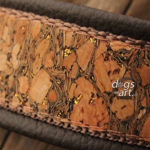 May include: A brown leather dog collar with a cork and gold glitter inlay. The collar has a stitched edge and the text "dogs art.net" is visible on the inlay.
