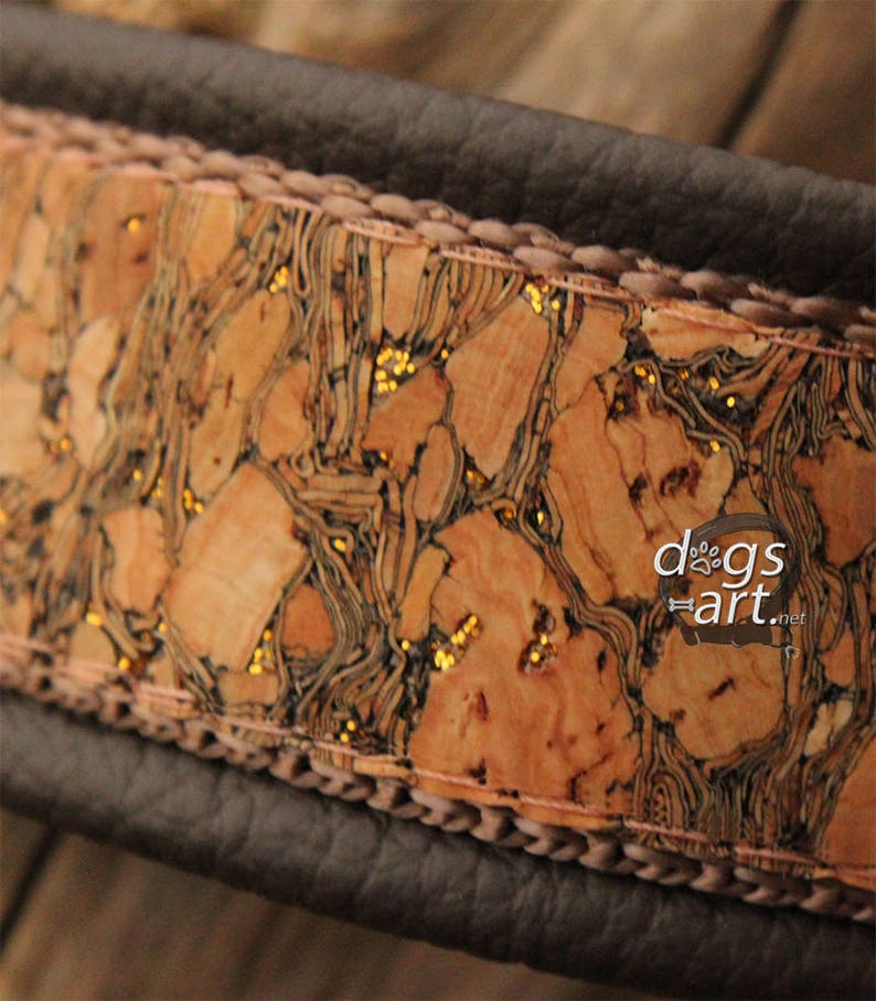 May include: A brown leather dog collar with a cork and gold glitter inlay. The collar has a stitched edge and the text "dogs art.net" is visible on the inlay.