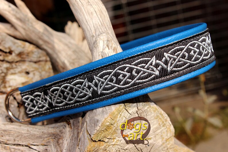 May include: A blue leather dog collar with a black and silver Celtic knot design. The collar has a silver D-ring.
