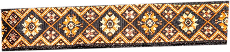 May include: Black and gold patterned fabric ribbon with a geometric design. The ribbon has a black border and a repeating pattern of diamond shapes with floral motifs.