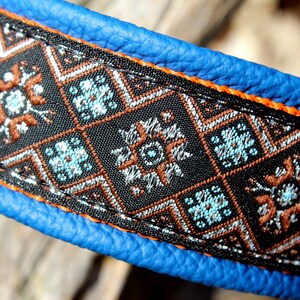 May include: A blue leather dog collar with orange stitching and a black and brown patterned fabric trim. The fabric trim features a geometric design with blue, silver, and brown accents.