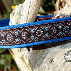 May include: A blue leather dog collar with a black and brown patterned trim. The collar has a silver buckle and is decorated with a geometric design.