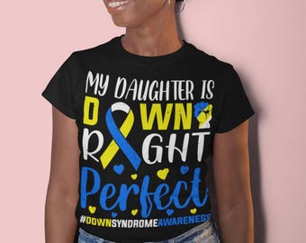 May include: Black t-shirt with the text "MY DAUGHTER IS DOWN RIGHT Perfect" in white, yellow, and blue. The shirt also includes the hashtag #DOWNSYNDROMEAWARENESS. The shirt is worn by a person wearing glasses and blue jeans.
