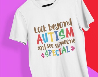 Può includere: Maglietta bianca con il testo "Look beyond autism and see someone special" in lettere colorate. La parola "autismo" è in colori arcobaleno e la parola "special" è circondata da simboli di pezzi di puzzle.
