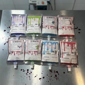 May include: Eight clear plastic pouches filled with colored liquids, labeled as blood bath products. Each pouch features a white label with text, barcodes, and graphics like dragons, aliens, and vampires, with colored drips printed on the top.