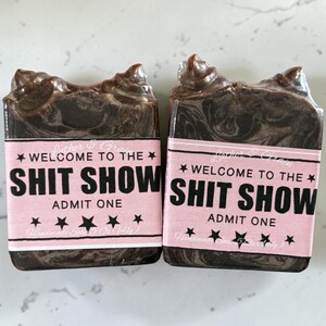 May include: Two handmade soaps with a dark brown, marbled appearance. Each soap has a pink label with the text "WELCOME TO THE SHIT SHOW, ADMIT ONE" in black. The soaps are 5 oz (141g) each.