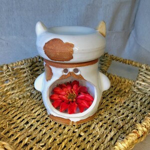May include: White ceramic oil burner shaped like a cartoon animal with brown accents and a red flower inside.