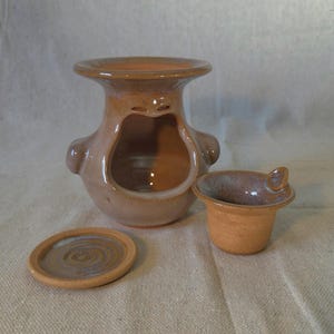 May include: A handmade ceramic set in shades of brown, featuring a large, open-faced vessel with two small handles, a small cup with a handle, and a small round plate. The set is likely for decorative or functional use.