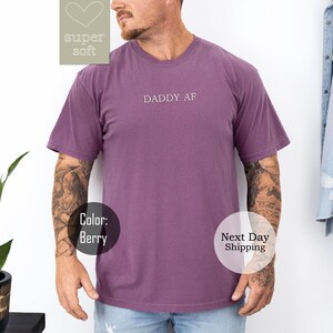 May include: A purple short-sleeved t-shirt with the text "Daddy AF" printed on the front.