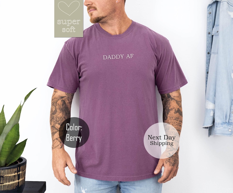 May include: A purple short-sleeved t-shirt with the text "Daddy AF" printed on the front.