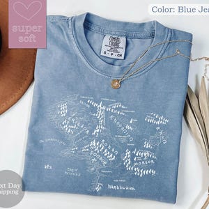 May include: A blue jean t-shirt with a white outline of the map of Middle-earth from The Lord of the Rings. The shirt has the text "COMFORT COLORS" and "S-P-CH" on the tag.