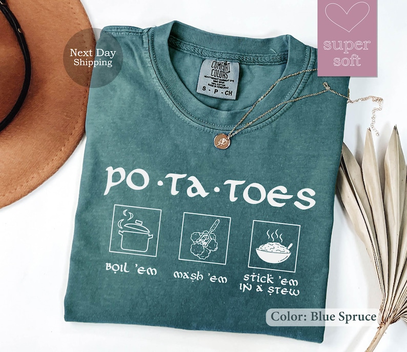 May include: Blue Spruce t-shirt with the word "potatoes" and cooking instructions. The shirt features illustrations of boiling, mashing, and stewing potatoes. A gold necklace with a pendant is on the shirt.