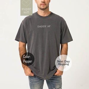 May include: A dark gray t-shirt with the text "DADDY AF" printed on the front.