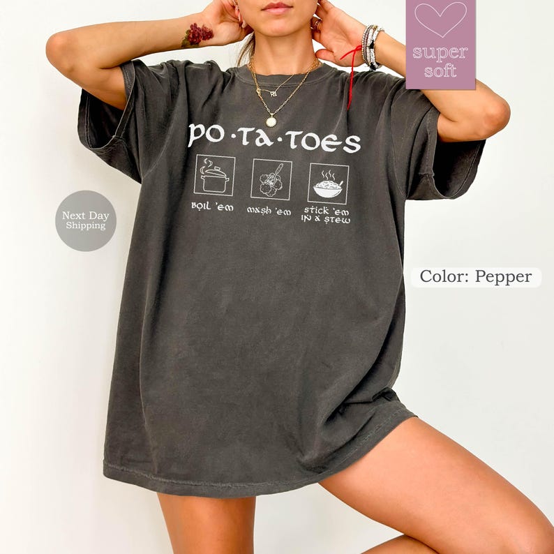 May include: Pepper-colored t-shirt with the word "potatoes" in white, along with illustrations and text: "boil 'em", "wash 'em", and "stick 'em in a stew". The shirt has a relaxed fit.
