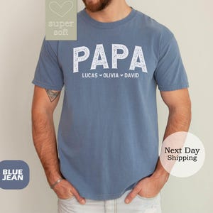 May include: Blue jean t-shirt with the word "PAPA" in white lettering and the names "Lucas, Olivia, David" underneath.