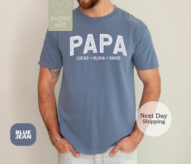 May include: Blue jean t-shirt with the word "PAPA" in white lettering and the names "Lucas, Olivia, David" underneath.