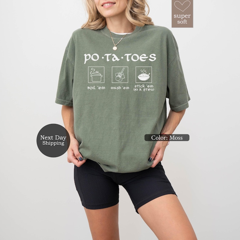 May include: Moss green t-shirt with the word "POTATOES" above three illustrated cooking methods: boil 'em, mash 'em, and stick 'em in a stew. The shirt is a soft material and has a relaxed fit.