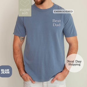 K&ouml;nnte beinhalten: Blaues Jeans-T-Shirt mit dem gestickten Text "Best Dad" auf der Vorderseite. Das Shirt ist super weich und hat ein Herz mit dem Text "super soft" auf der linken Brustseite.