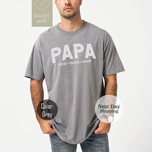 May include: Gray t-shirt with the word "PAPA" printed in white with the names Lucas, Olivia, and David underneath.