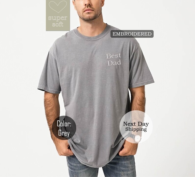 K&ouml;nnte beinhalten: Graues T-Shirt mit dem gestickten Text "Best Dad" auf der Vorderseite. Das Shirt ist aus weichem, bequemem Stoff.
