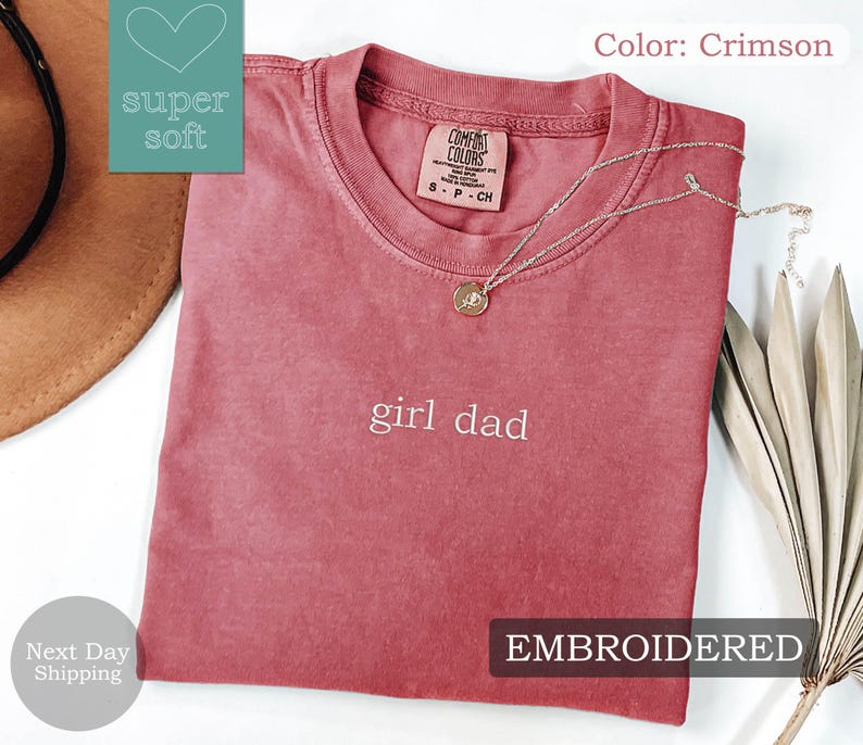 K&ouml;nnte beinhalten: Ein T-Shirt in Rot mit der Aufschrift "girl dad", die in Wei&szlig; gestickt ist. Das Shirt ist aus einem weichen, bequemen Stoff.