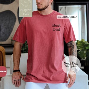 K&ouml;nnte beinhalten: Ein T-Shirt in Rot mit dem gestickten Text "Best Dad" auf der Vorderseite. Das T-Shirt ist aus superweichem Material.