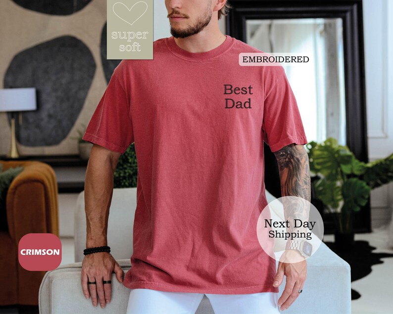 K&ouml;nnte beinhalten: Ein T-Shirt in Rot mit dem gestickten Text "Best Dad" auf der Vorderseite. Das T-Shirt ist aus superweichem Material.
