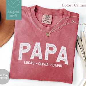 May include: Crimson red t-shirt with the word "PAPA" in white with a decorative floral design. The names "LUCAS", "OLIVIA", and "DAVID" are written below in white.