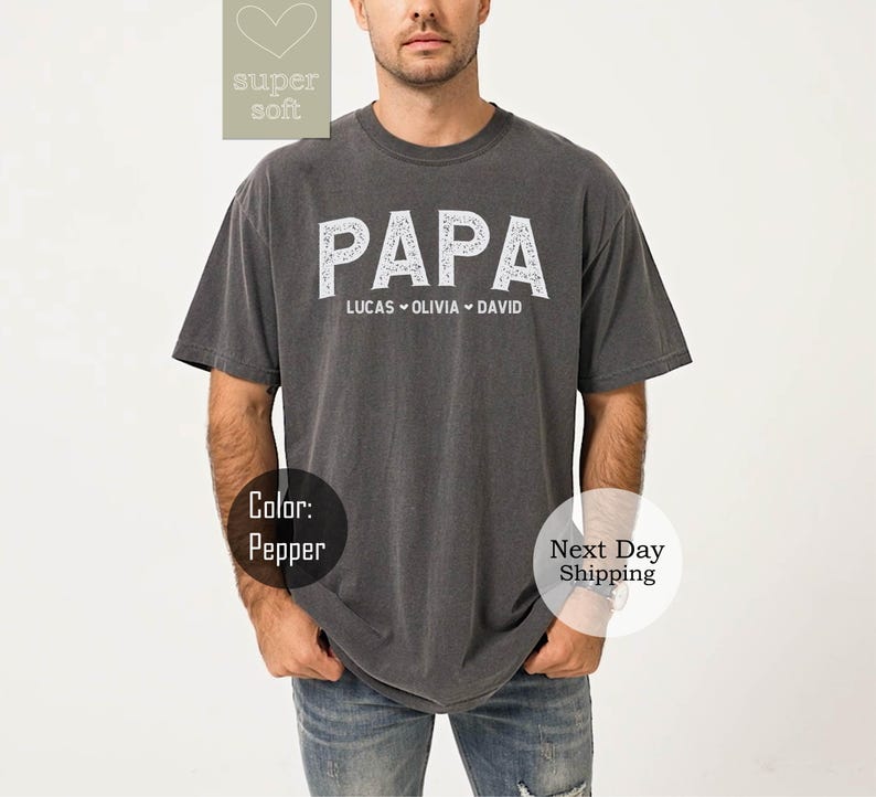 May include: A dark gray t-shirt with the word "PAPA" in white lettering. The names "Lucas", "Olivia", and "David" are printed below the word "PAPA".