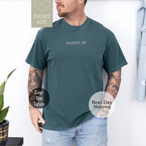 May include: A dark green t-shirt with the text "DADDY AF" printed on the front. The shirt is made of a soft, comfortable material.