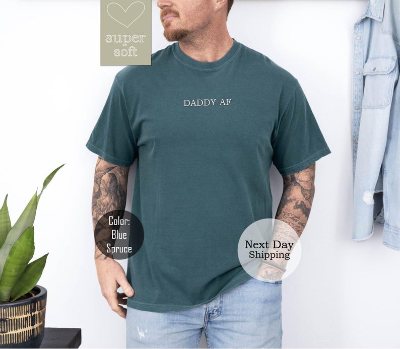 May include: A dark green t-shirt with the text "DADDY AF" printed on the front. The shirt is made of a soft, comfortable material.