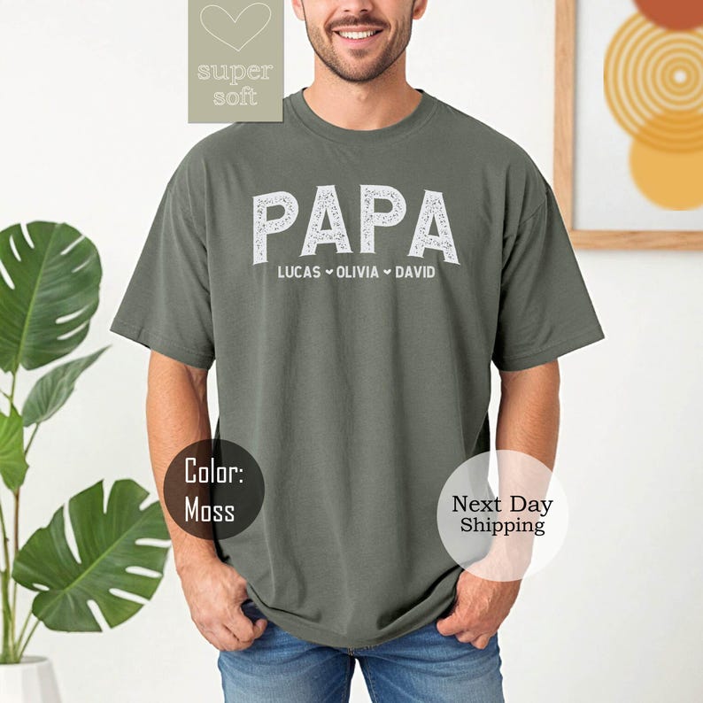 May include: A green t-shirt with the word "PAPA" in white text. Below the word "PAPA" is the text "LUCAS OLIVIA DAVID" in smaller white text.