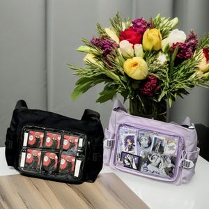 May include: Two black and purple bags with clear plastic windows. The bags have adjustable straps and are decorated with colorful cartoon characters. The bags are sitting on a wooden surface in front of a bouquet of flowers.