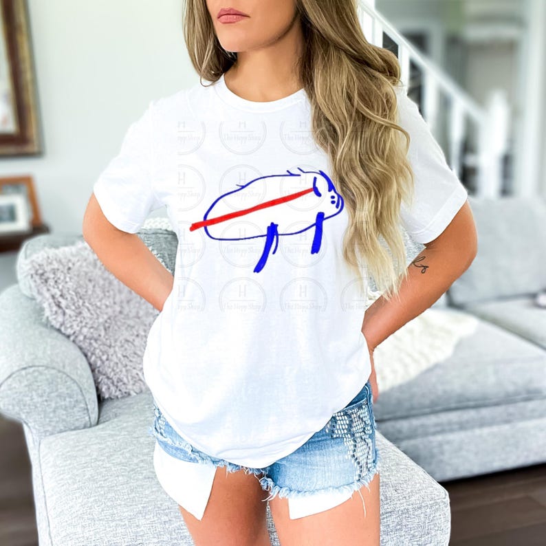 Pu&ograve; includere: Una t-shirt bianca a maniche corte con un disegno al tratto blu minimalista di un bisonte, attraversato da una linea rossa orizzontale audace al centro del corpo. La maglietta &egrave; abbinata a pantaloncini di jeans azzurri con bordi sfrangiati.