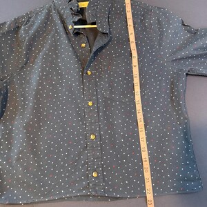 May include: Navy blue button-down shirt with a ruffle collar and small white and red triangle pattern. The shirt has gold-colored buttons and a single chest pocket. A measuring tape shows the shirt is approximately 26 inches long.