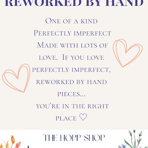 May include: A cream-colored sign with the text "REWORKED BY HAND" in dark blue. The sign includes the phrases "ONE OF A KIND", "PERFECTLY IMPERFECT", and "MADE WITH LOTS OF LOVE". Two pink heart illustrations are on the sign. The shop name "THE HOPP SHOP" is at the bottom.