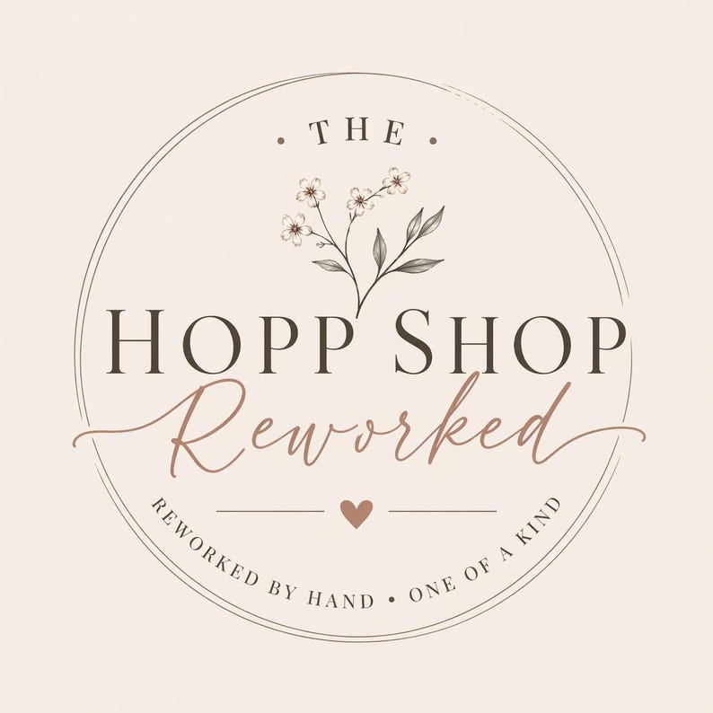 May include: A circular logo with the text "THE" at the top, and "HOPP SHOP" in a serif font. Below, the word "Reworked" is in a cursive font. The logo includes a floral illustration and the text "REWORKED BY HAND &bull; ONE OF A KIND".