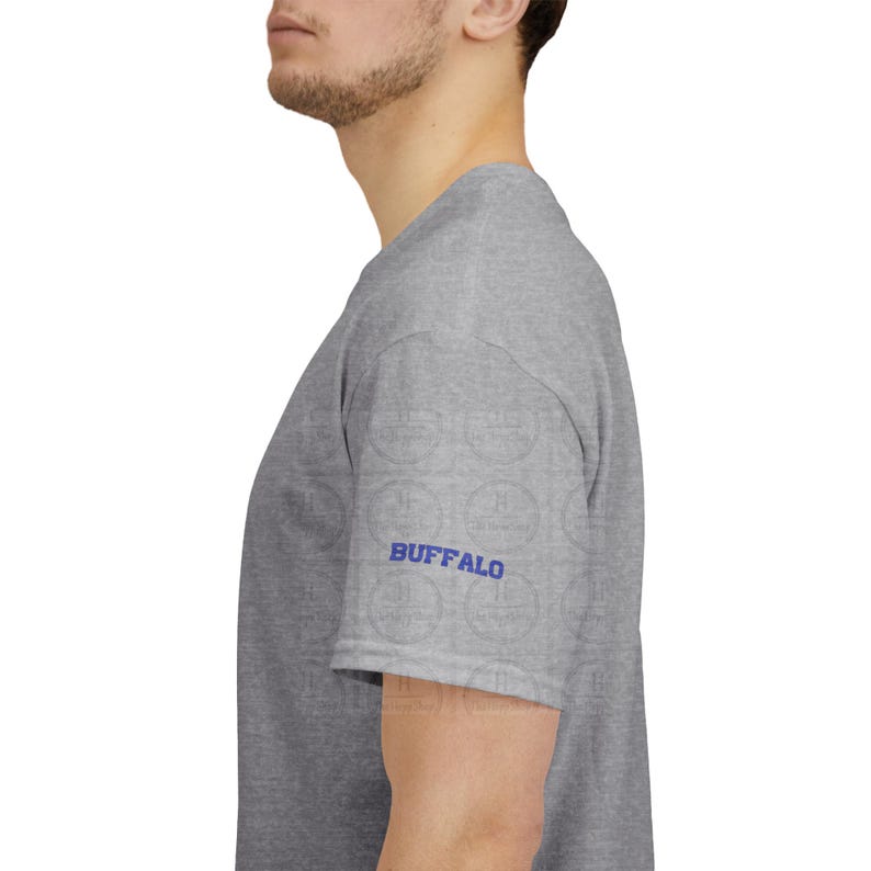 Pu&ograve; includere: Una t-shirt grigio m&eacute;lange a maniche corte con la parola BUFFALO stampata in lettere maiuscole blu brillante sulla manica. Il capo &egrave; mostrato di profilo, evidenziando il dettaglio della manica e la trama del tessuto grigio neutro.