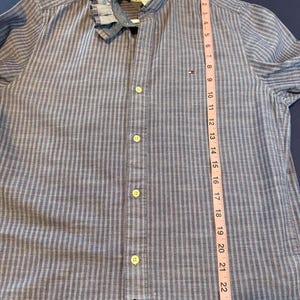 May include: Blue and gray striped button-down shirt with a ruffled collar. The shirt has a Tommy Hilfiger logo and measures approximately 24 inches in length. The shirt has a classic design with a modern twist.