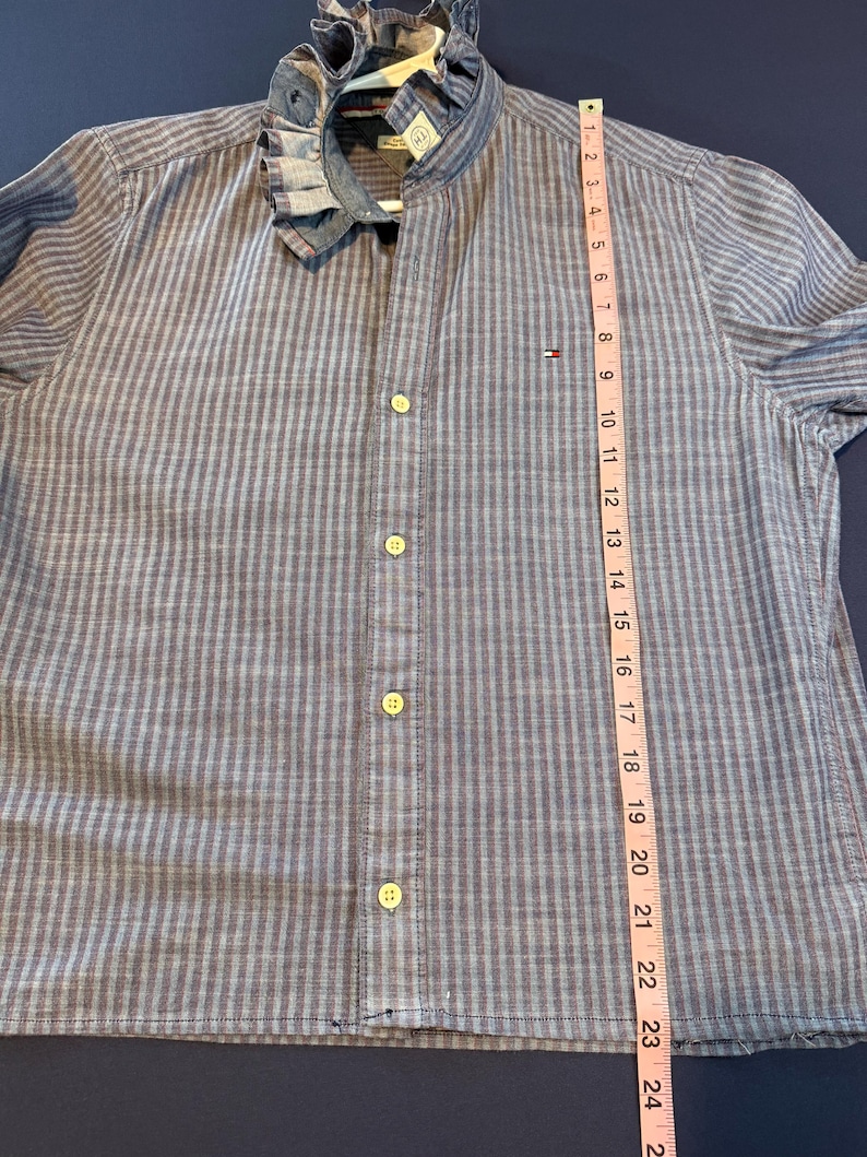 May include: Blue and gray striped button-down shirt with a ruffled collar. The shirt has a Tommy Hilfiger logo and measures approximately 24 inches in length. The shirt has a classic design with a modern twist.