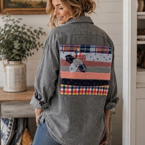Può includere: Una camicia a maniche lunghe grigio antracite con bottoni e una grande toppa rettangolare sulla schiena. La toppa è composta da strisce orizzontali di vari tessuti con motivi a quadri, a righe e floreali in rosso, blu, giallo e rosa.