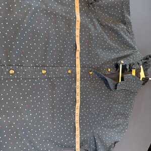 May include: A navy blue button-down shirt with a white and red triangle pattern. The shirt has gold-colored buttons and a ruffled collar. The shirt measures approximately 26 inches in length.