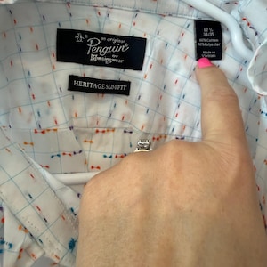 May include: White button-down shirt with a grid pattern and colorful accents. The shirt features the "Penguin" logo and "Heritage Slim Fit" label. The tag indicates a size of 17 1/2 and 34/35, made of 60% cotton and 40% polyester.