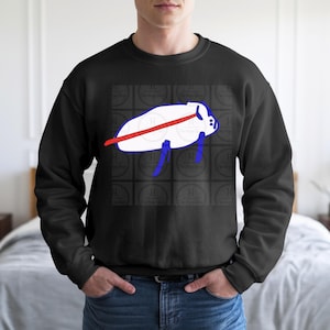 May include: Black crewneck sweatshirt featuring a white and blue graphic design. The graphic depicts a stylized creature with a red stripe across its body. The design is centered on the chest.