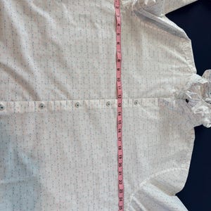 May include: White button-down shirt with a subtle grid pattern of blue, red, and pink dashes. The shirt has a ruffled collar and cuffs. A pink measuring tape shows the shirt is approximately 29 inches long.