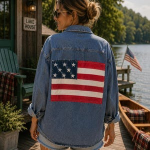 May include: A blue denim button-down shirt featuring a large rectangular patch of the American flag on the back. The shirt has a classic collar, long sleeves with rolled cuffs, and a relaxed fit, showcasing a distressed fabric texture.