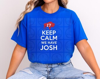 Puede incluir: Una camiseta azul brillante de manga corta con una silueta de búfalo roja que contiene el número 17, seguida del texto blanco "KEEP CALM WE HAVE JOSH" impreso en una fuente sans-serif en negrita en el centro del pecho.